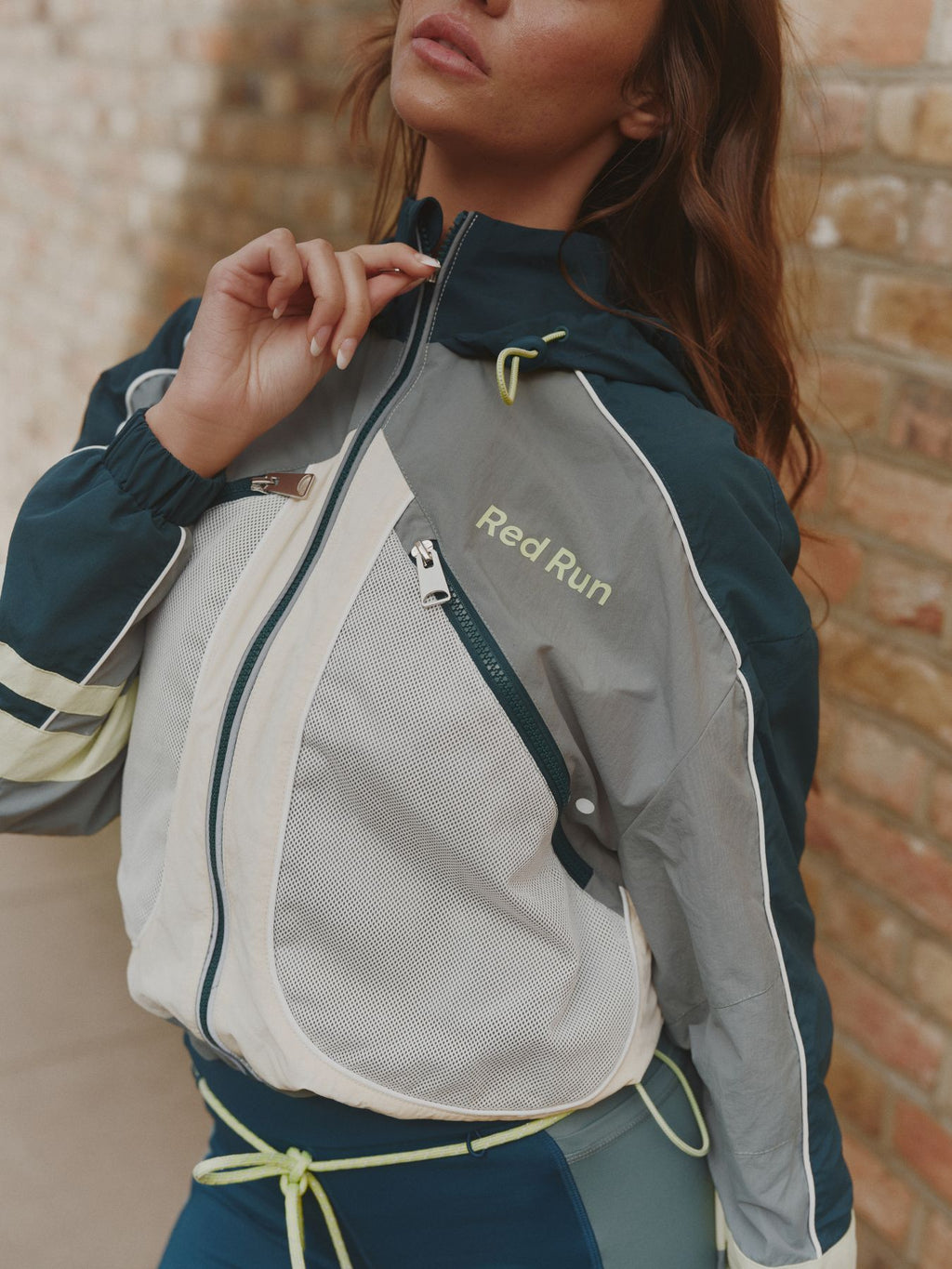 Person wearing a sports jacket with 'Red Run' branding against a brick wall.