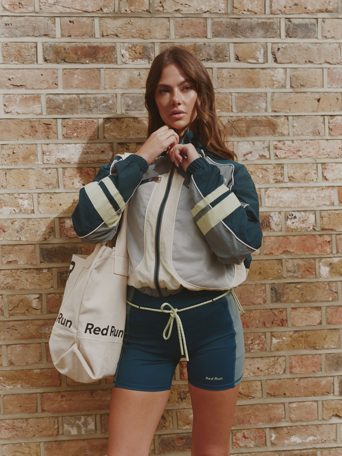 Woman in athletic wear holding a bag against a brick wall