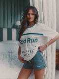 Woman wearing a 'Red Run' t-shirt and shorts in a bedroom setting