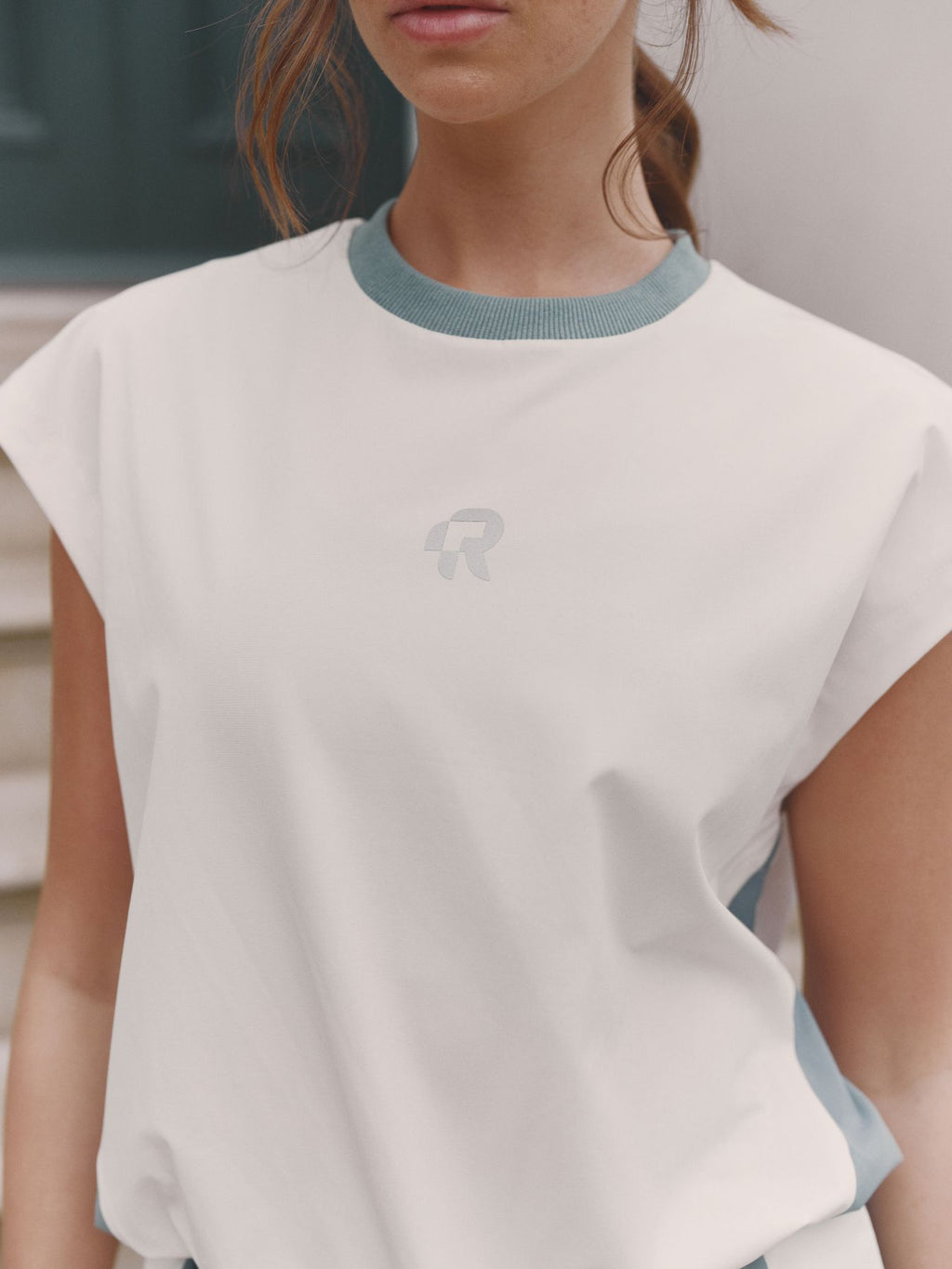 Person wearing a white top with blue trim and a logo on a blurred background