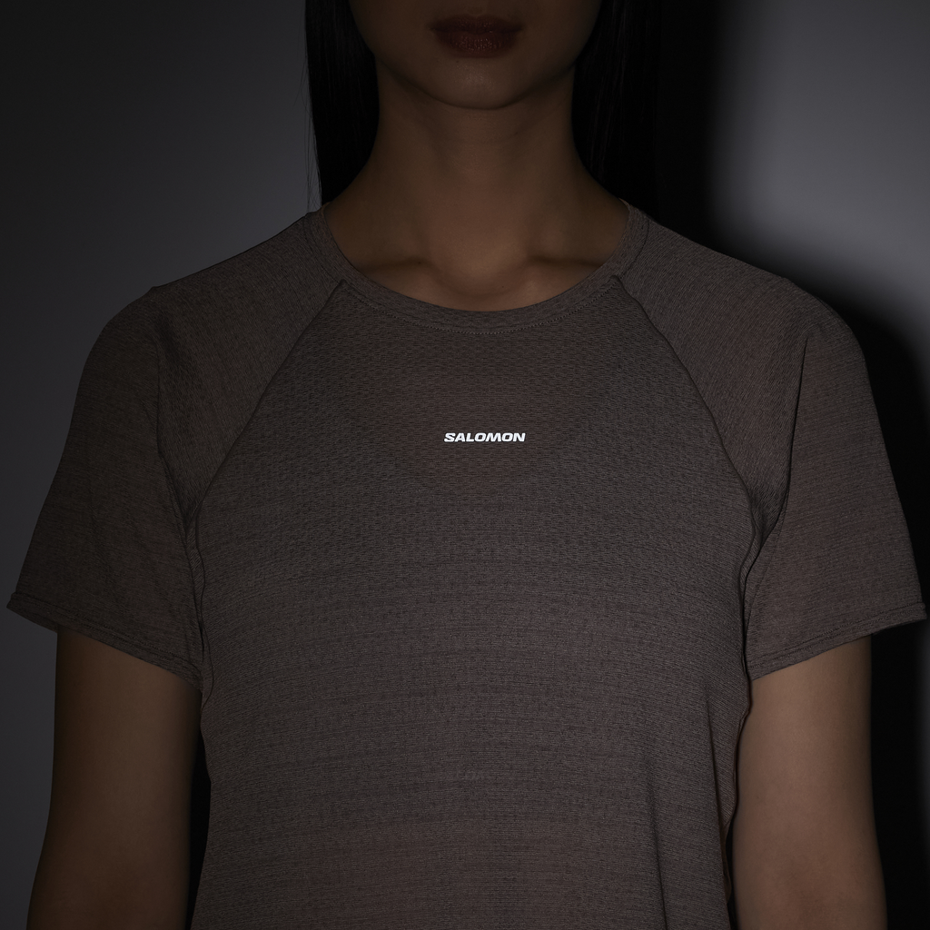 Person wearing a dark gray t-shirt with 'Salomon' logo on a dark background