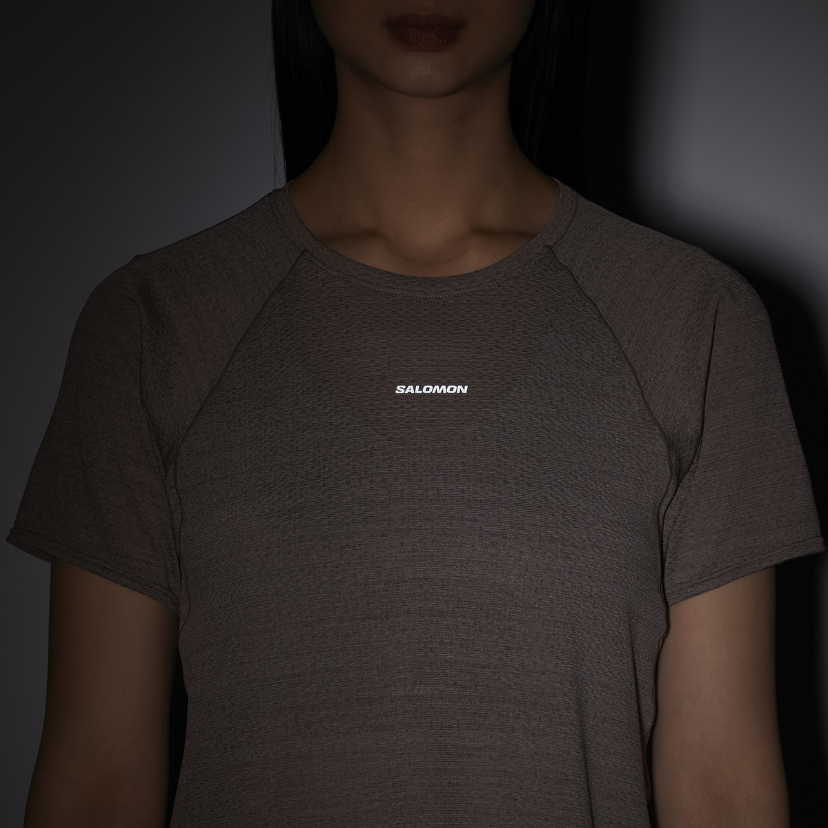 Person wearing a dark gray t-shirt with 'Salomon' logo on a dark background