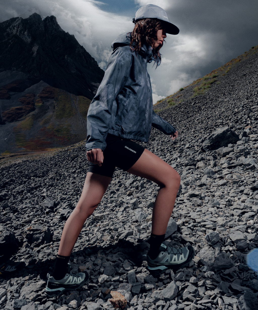 Person hiking on a rocky mountain trail wearing outdoor gear.