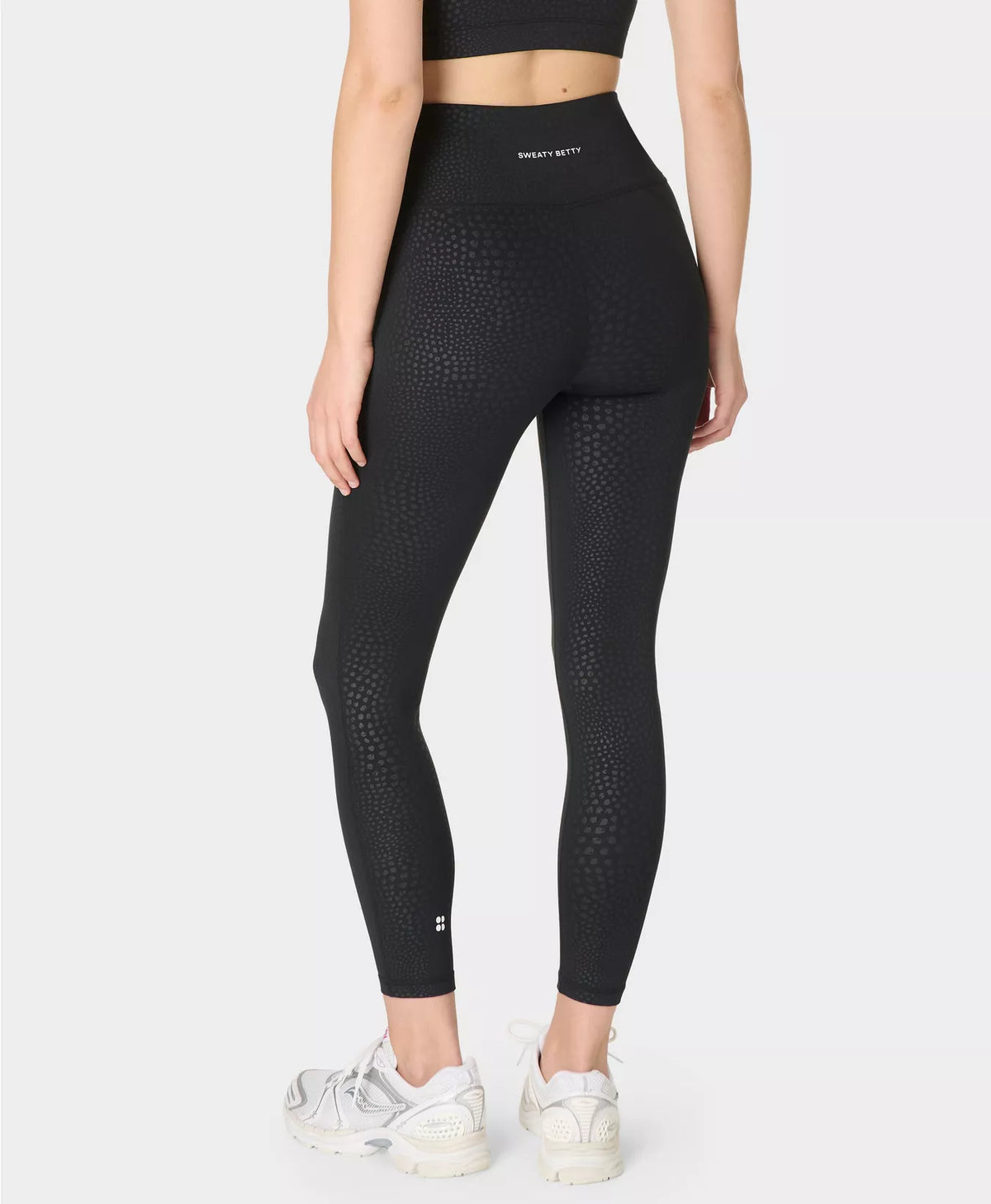 Person wearing black leggings with a subtle pattern on a white background