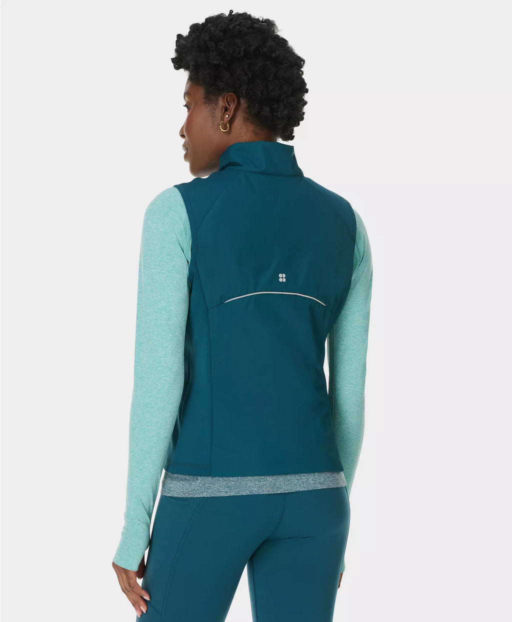 Person wearing a teal vest over a light blue long-sleeve shirt and pants on a white background