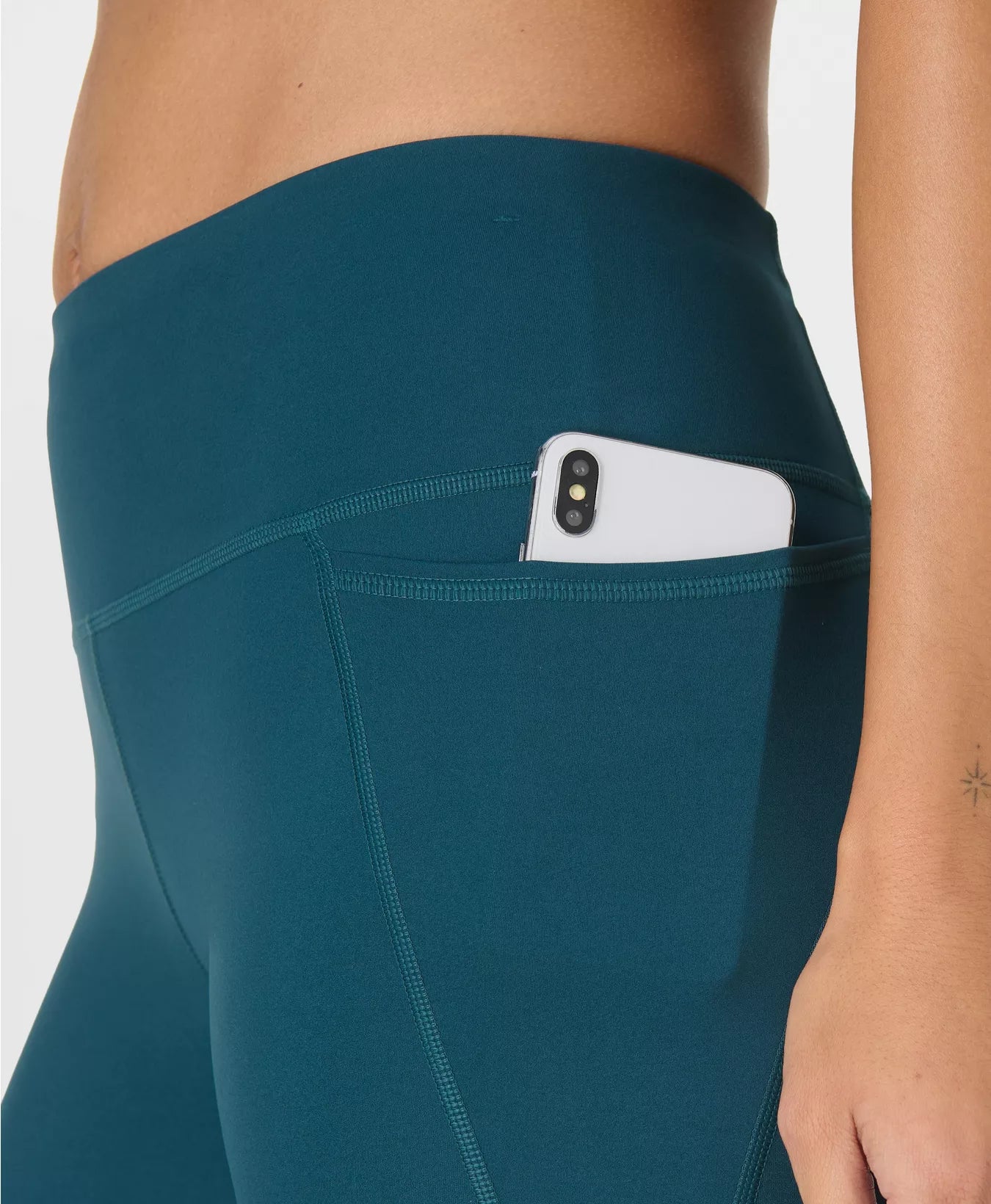 Teal leggings with a pocket holding a phone on a white background