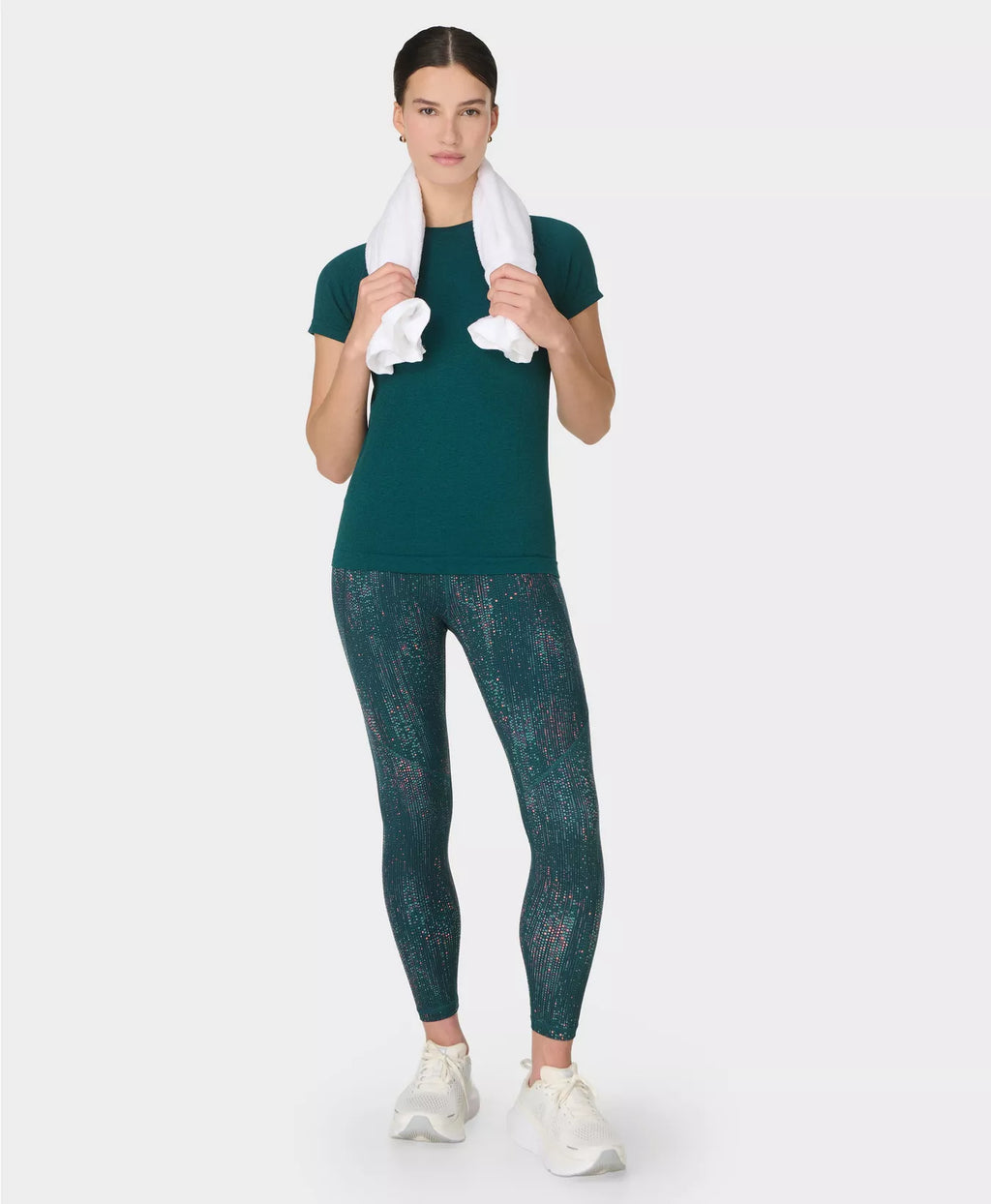 Woman in green athletic outfit holding a white towel on a white background