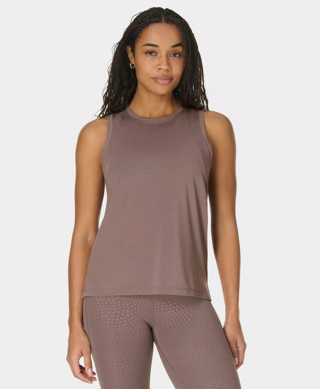 Woman wearing a brown sleeveless top and leggings on a white background
