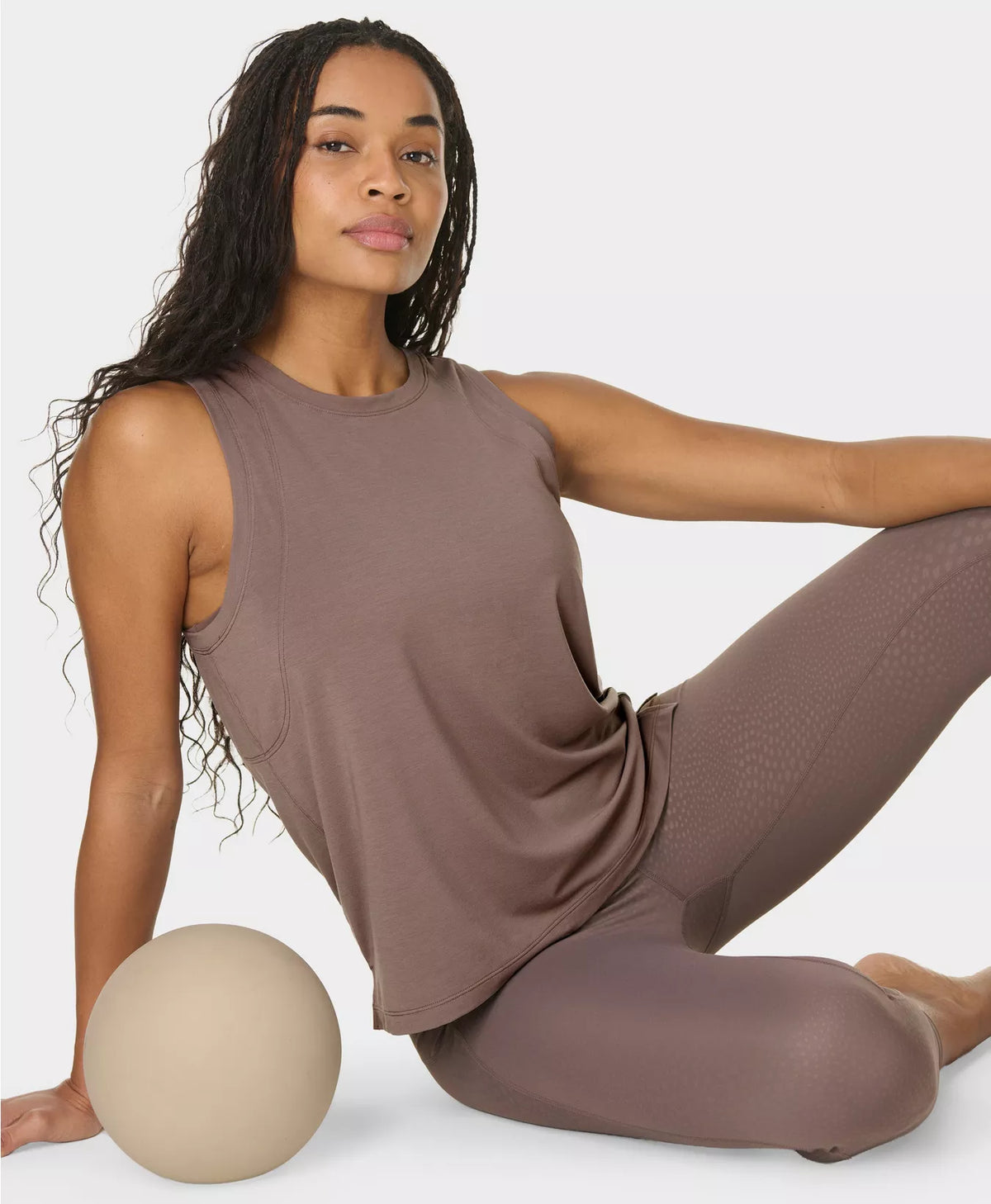 Woman in brown athletic wear posing with a ball on a white background