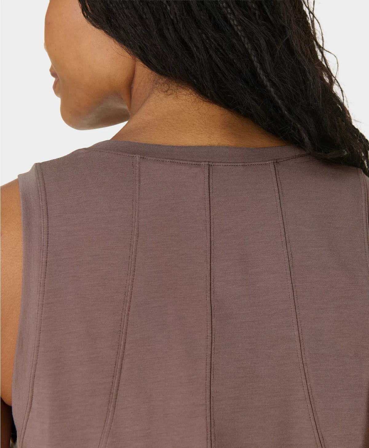 Close-up of a person wearing a sleeveless brown top with a neutral background
