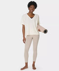 Woman holding a yoga mat wearing a white top and beige leggings on a white background
