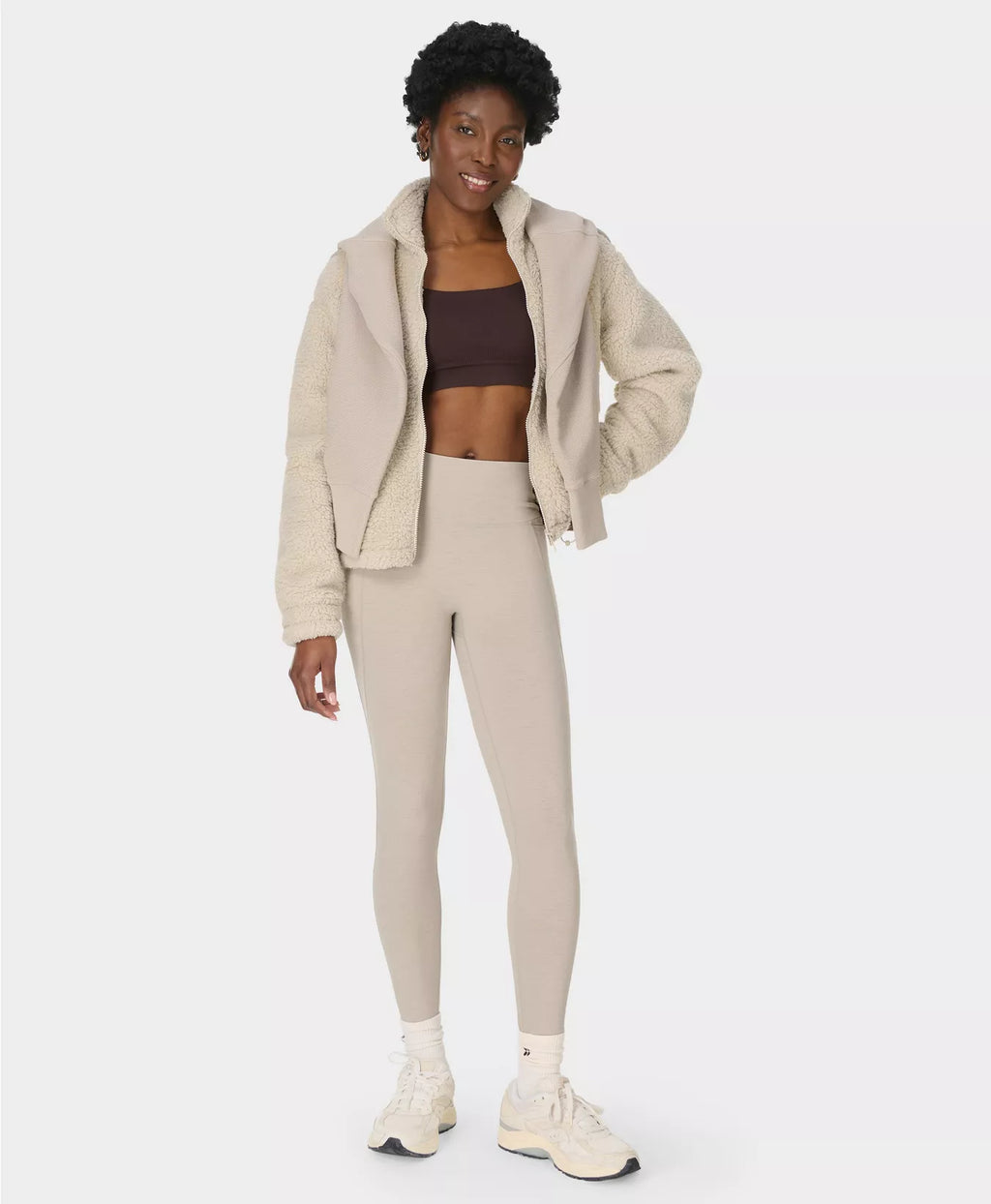 Woman wearing a beige hoodie and leggings set on a white background
