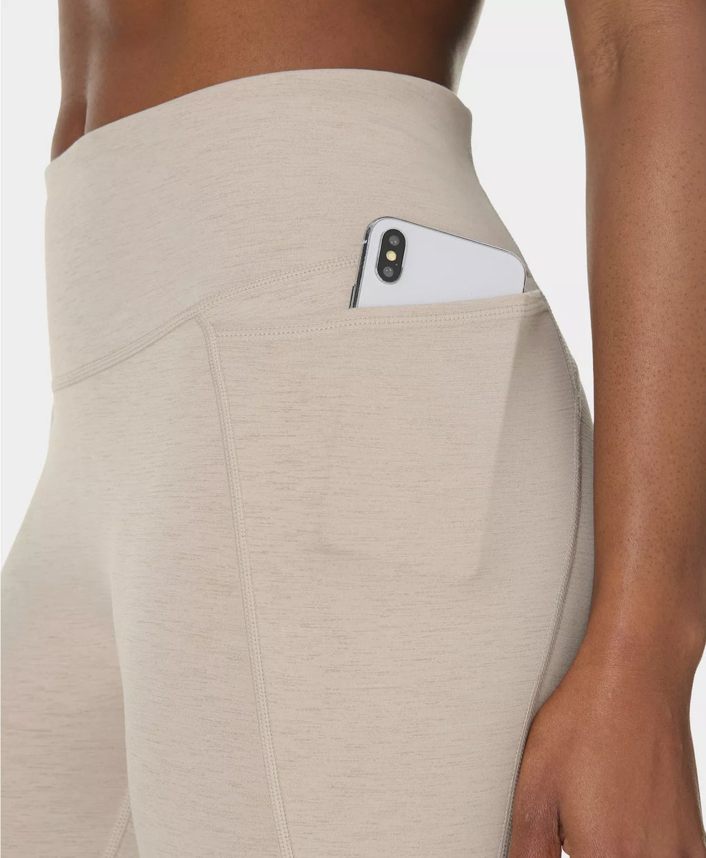 Beige leggings with a pocket holding a phone on a neutral background