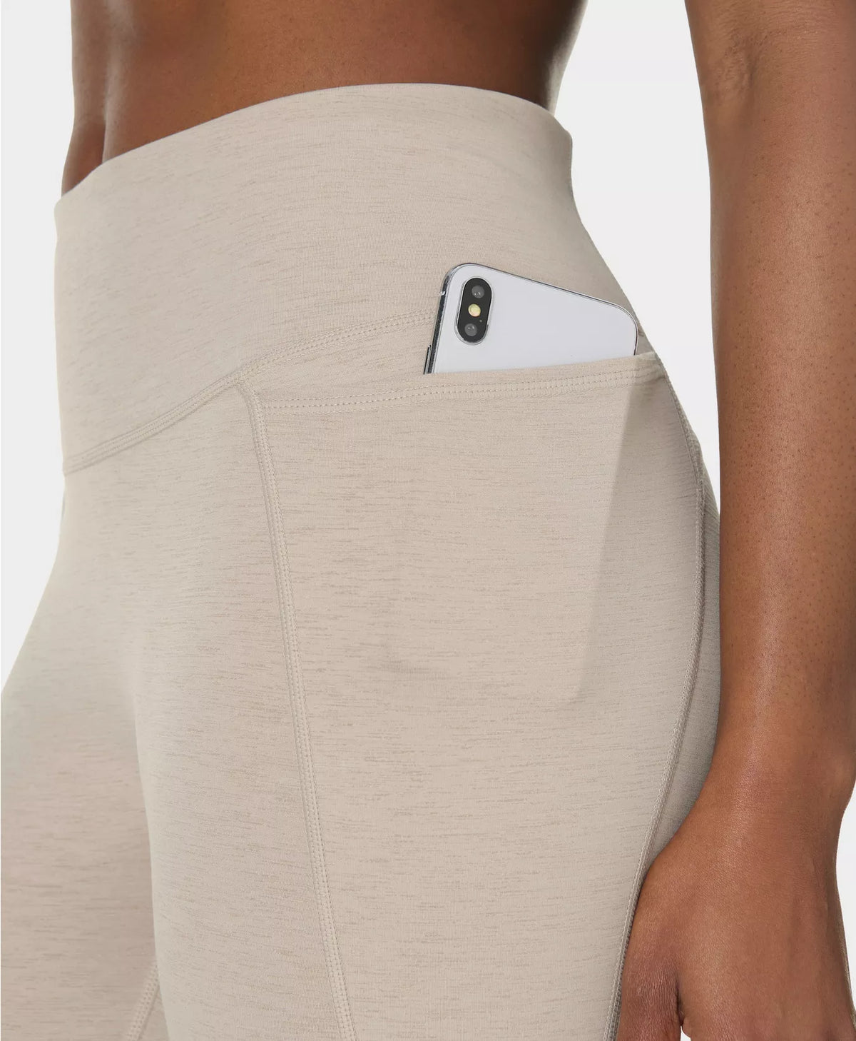 Beige leggings with a pocket holding a phone on a neutral background