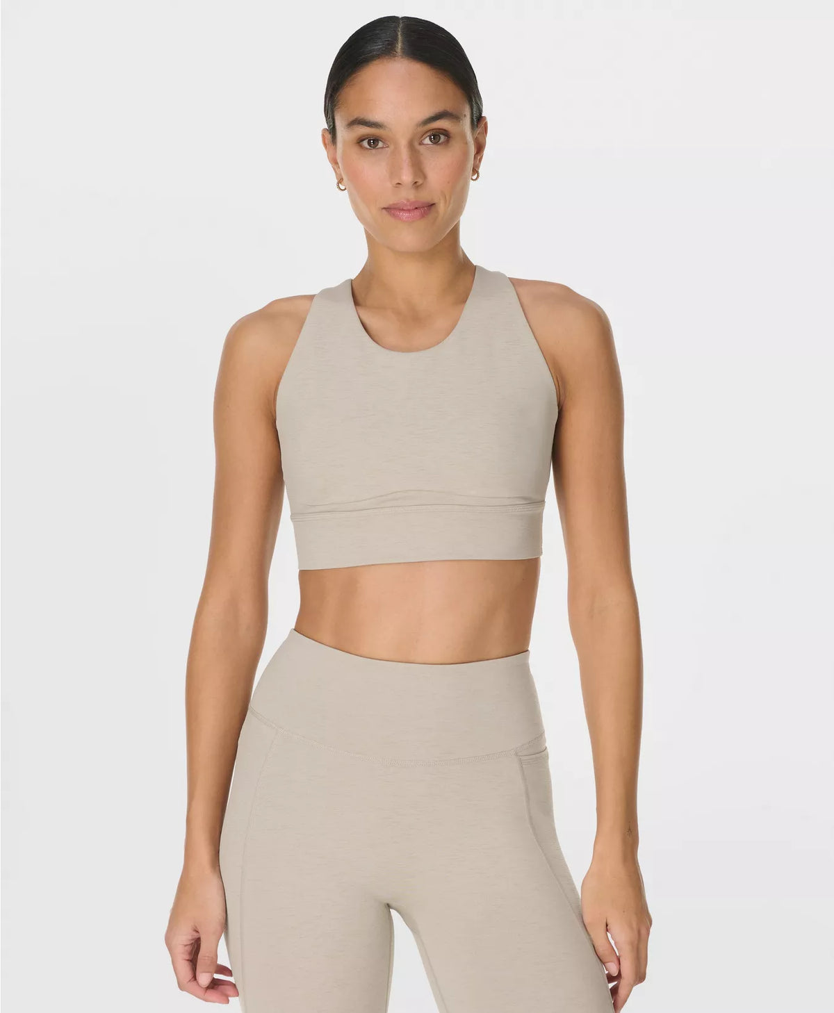 Woman wearing a beige sports bra and leggings on a white background