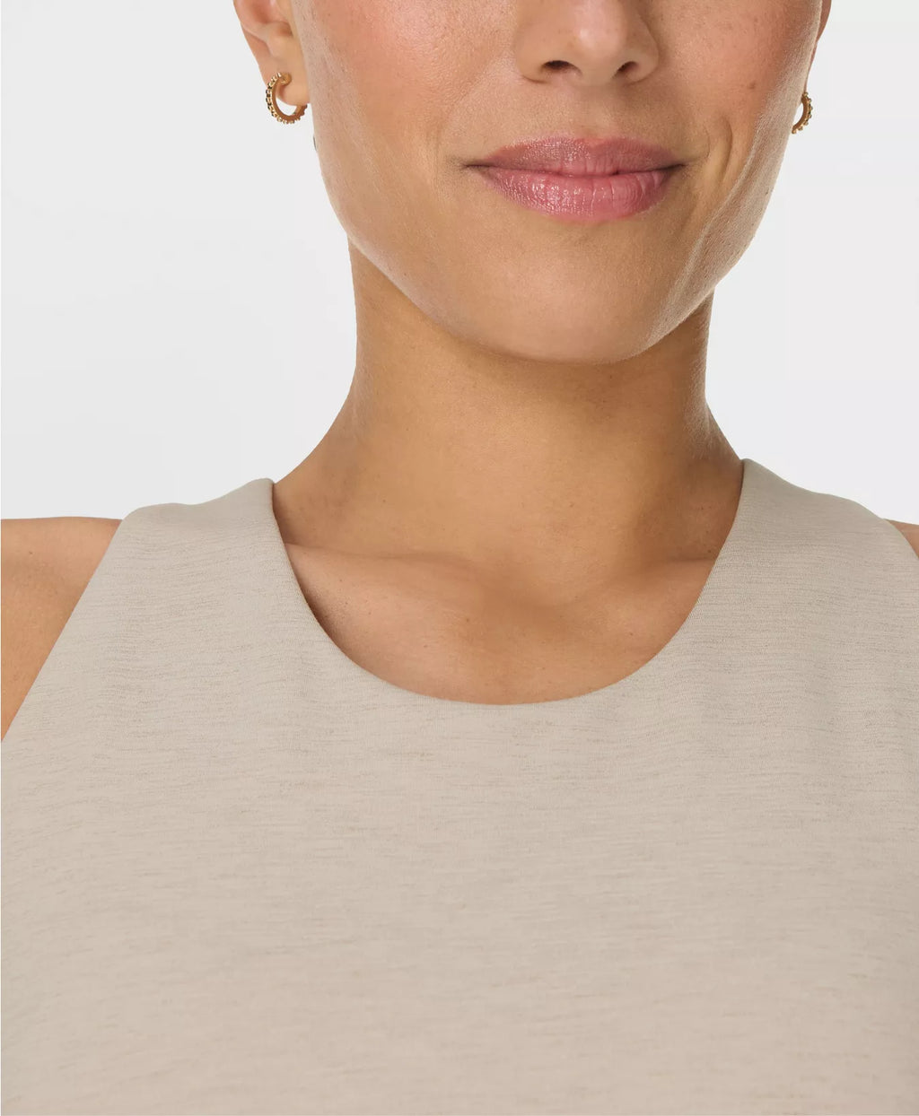 Close-up of a person wearing a beige sleeveless top against a light background