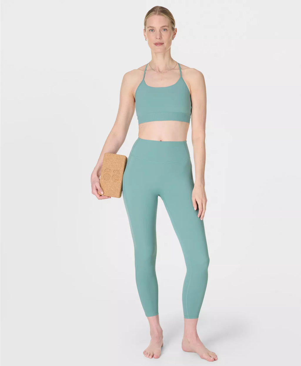 Woman wearing a matching green sports bra and leggings set on a white background