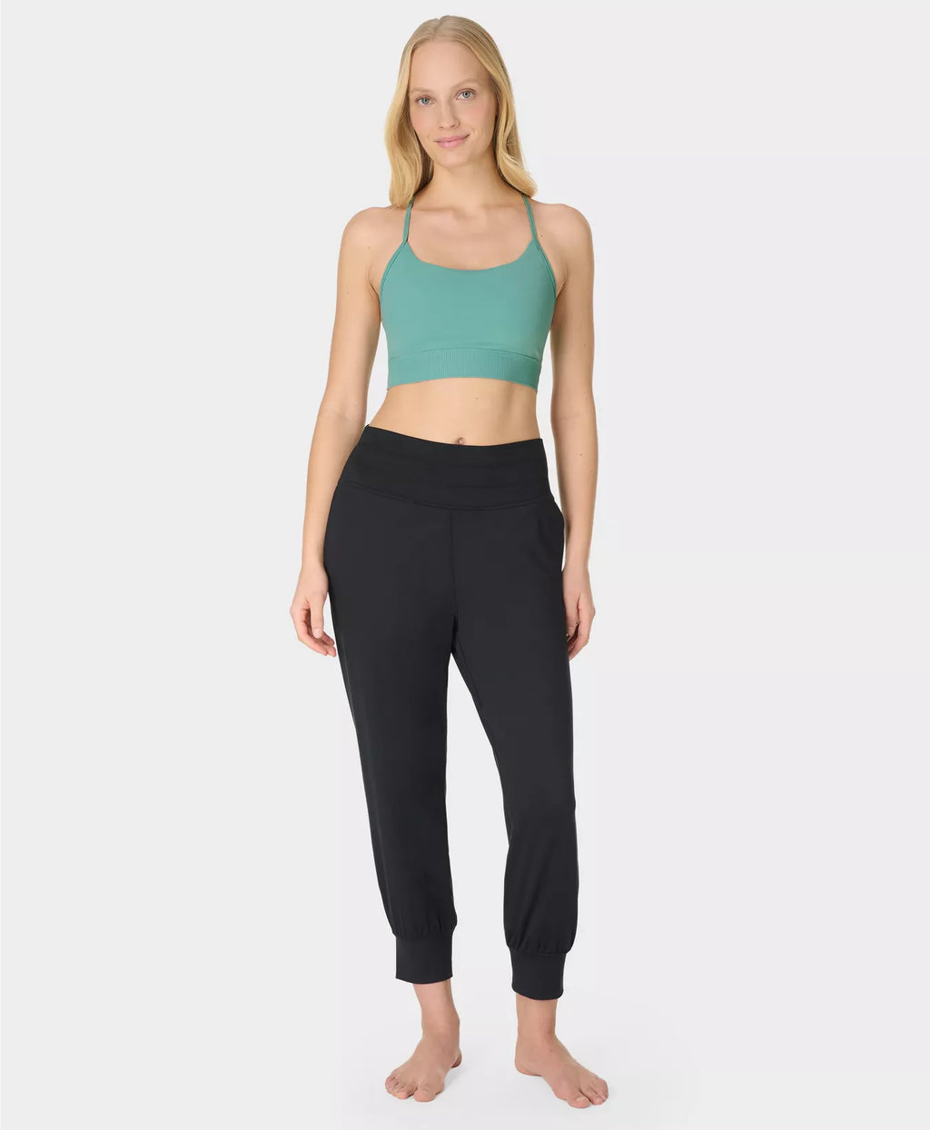 Woman wearing a green sports bra and black leggings on a white background
