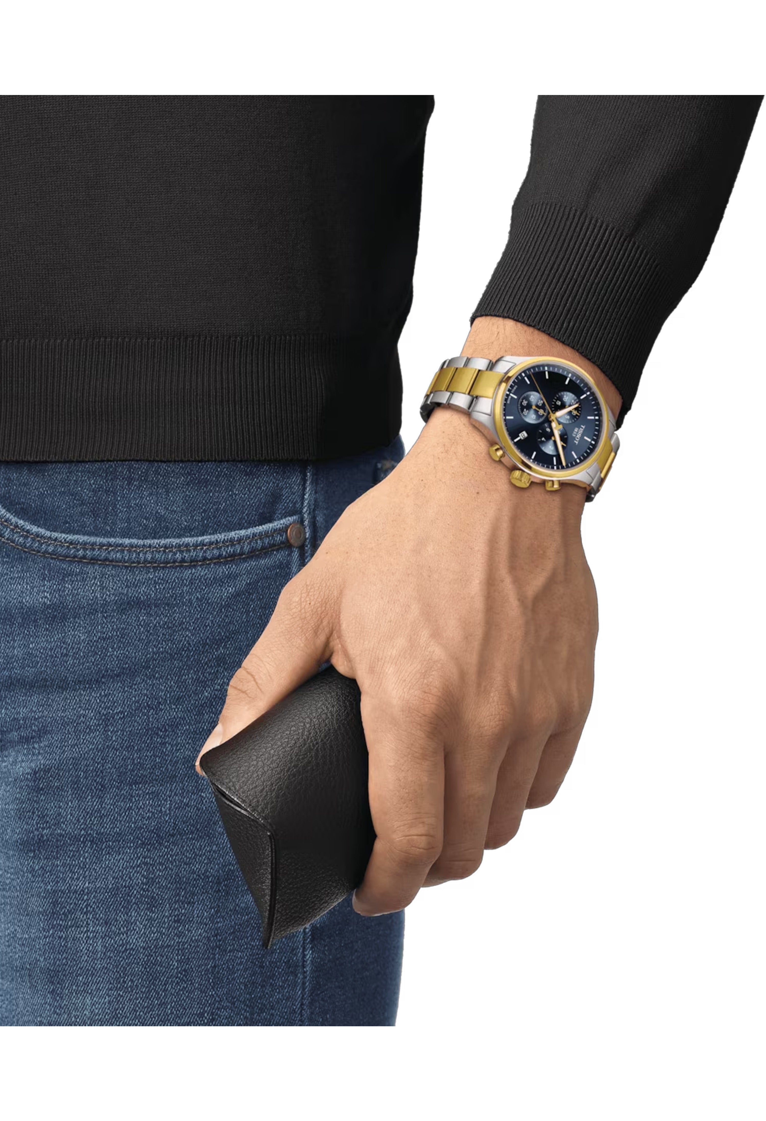 Man wearing a Tissot Chronograph XL Classic watch with a black dial and gold accents, holding a wallet.