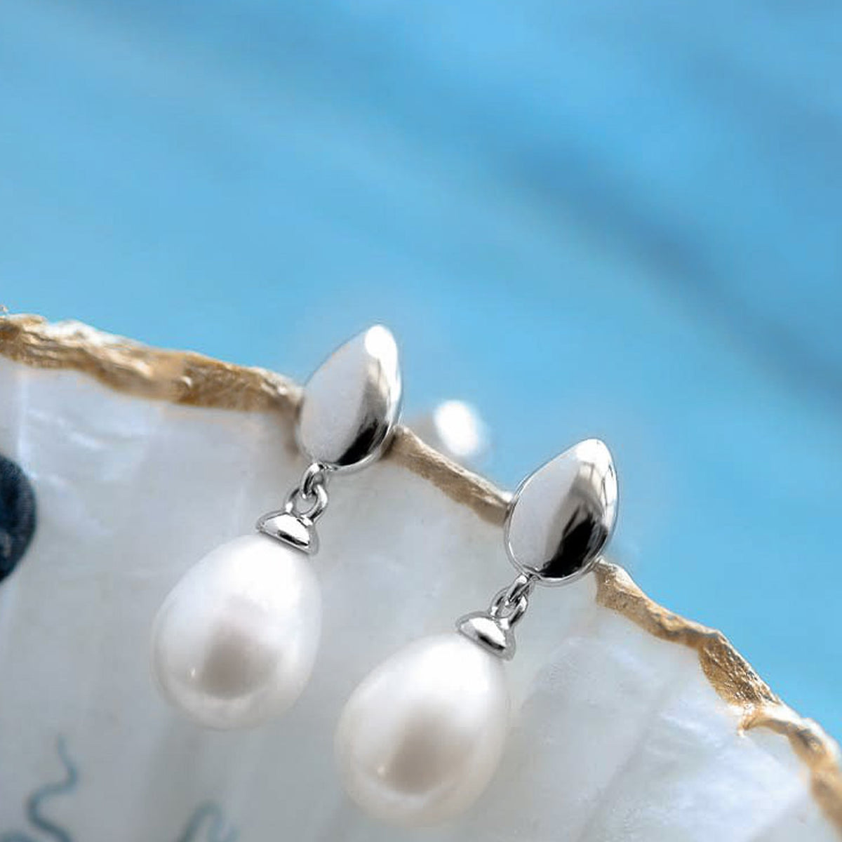 Elegant Kit Heath pearl earrings displayed, showcasing the Coast Pebble design in polished sterling silver. Jewelry detail.