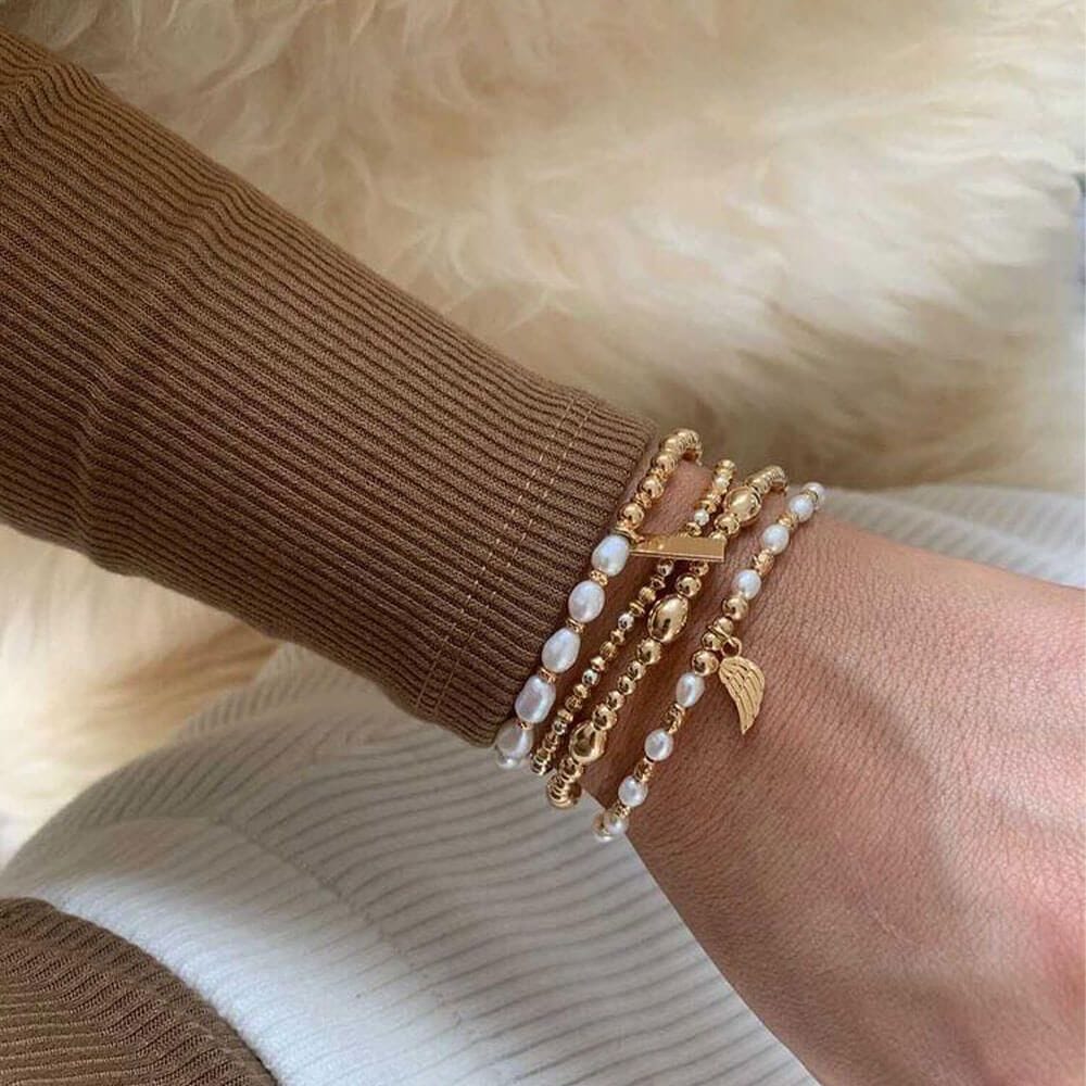 A woman's arm wearing a brown sweater and several gold and pearl beaded bracelets.
