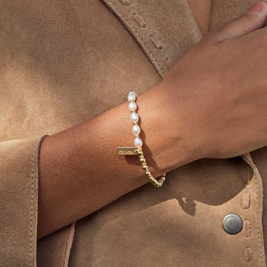 Hand with pearl and gold beaded bracelet on brown suede jacket.