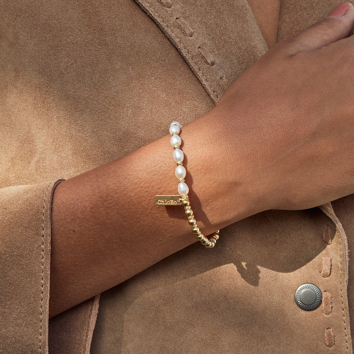 Hand with pearl and gold beaded bracelet on brown suede jacket.