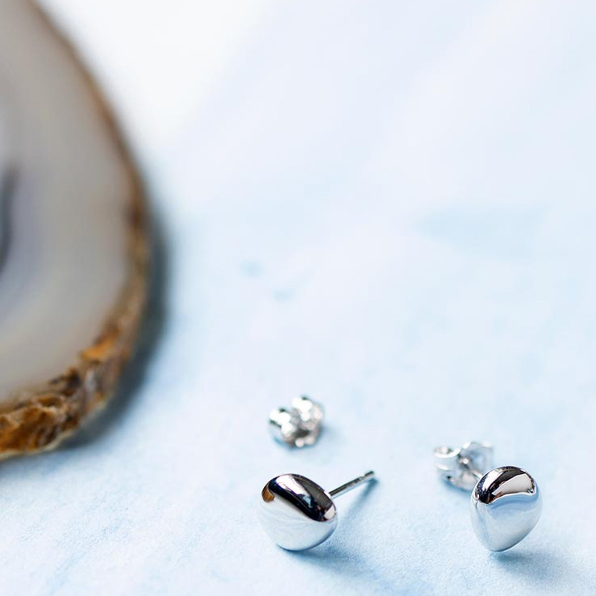 Close-up showing Kit Heath Coast Pebbles silver stud earrings with pebble-shaped design, showcasing fine jewelry detail.