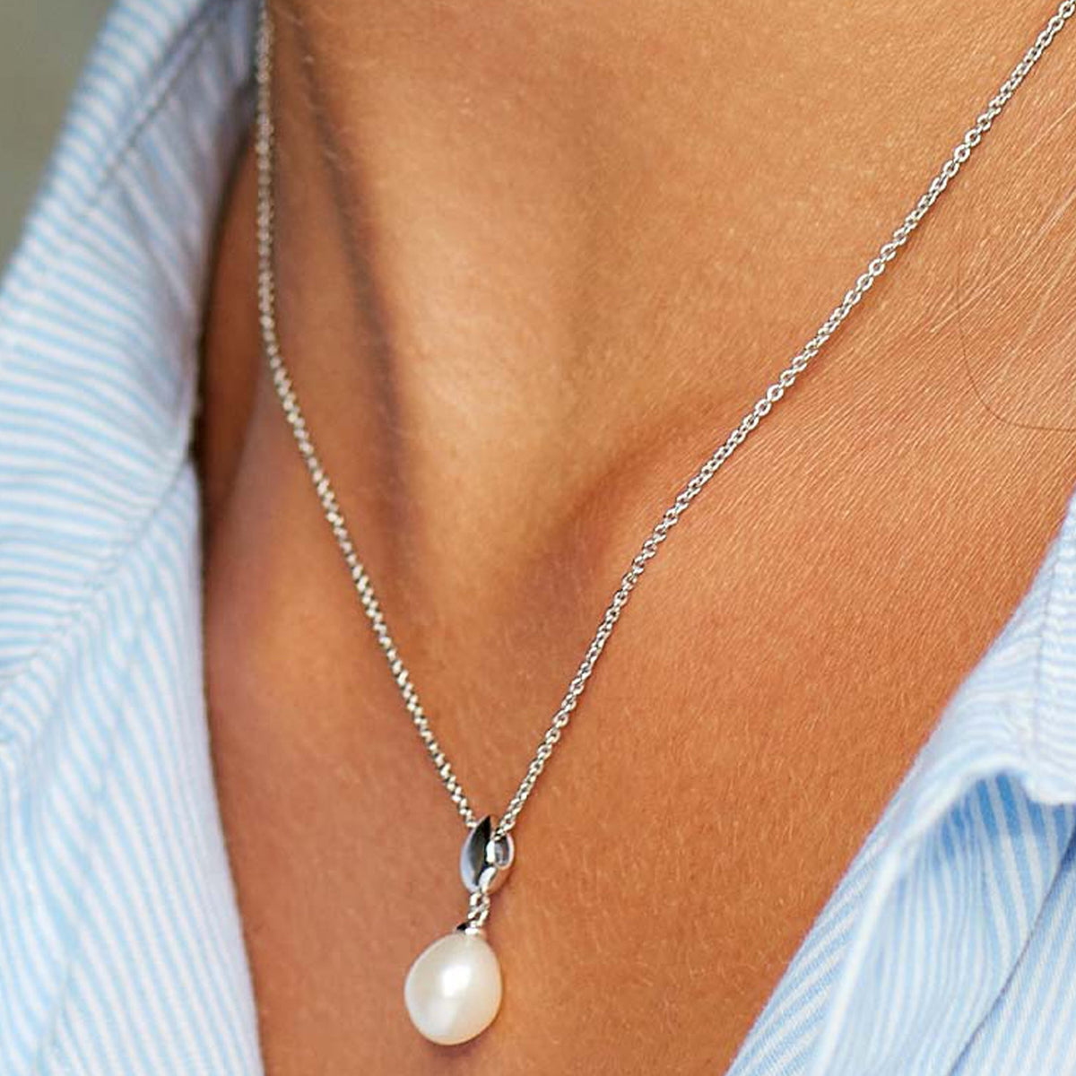 Woman wearing a Kit Heath pearl necklace. Elegant Coast Pebble pearl pendant on a delicate sterling silver chain.