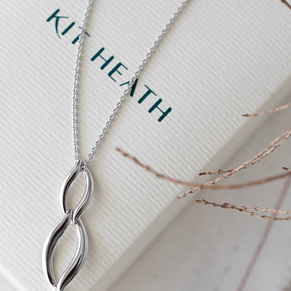 Kit Heath Entwine silver necklace on gift box. Classic designer jewelry showcased for online retail with "KIT HEATH"