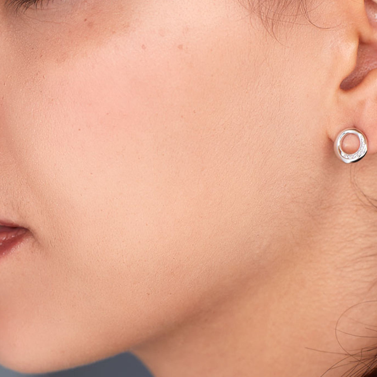 Close-up of a woman wearing Kit Heath silver stud earrings, showcasing the Bevel Cirque design with pave CZ detail.