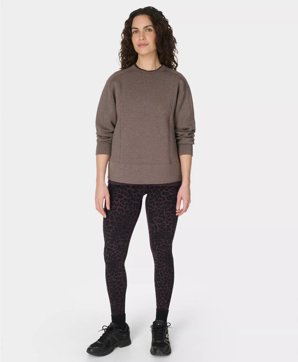 Woman wearing a brown sweater and black patterned leggings on a white background