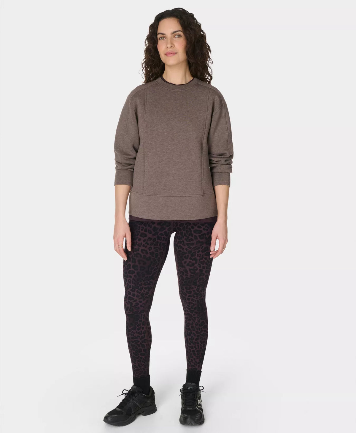 Woman wearing a brown sweater and black patterned leggings on a white background