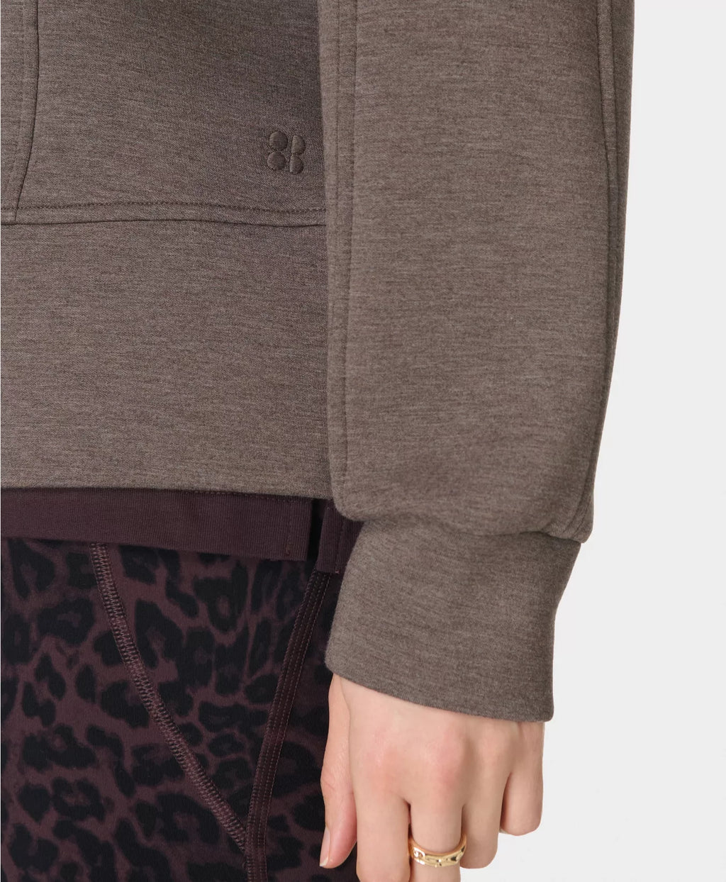 Close-up of a person wearing a gray hoodie with a leopard print garment underneath on a white background.