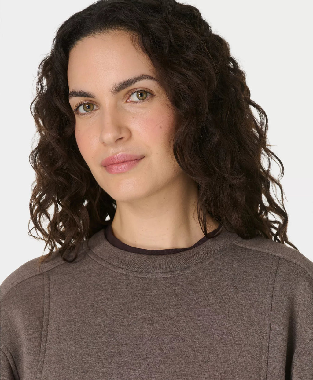 Woman with curly hair wearing a brown sweater against a white background