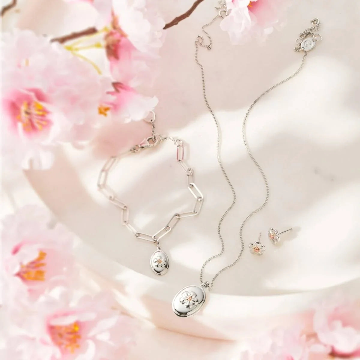 Silver jewelry set with floral accents on a white surface with pink flowers.